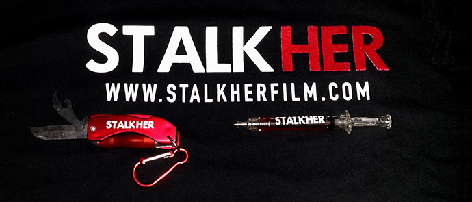 Close up of Stalkher grab bag of promotional gear: stalking utility knife, novelty syringe pen and one of the at least three t-shirt variations close up of stalkher grab bag of promotional gear: stalking utility knife, novelty syringe pen and one of at least three tshirt variations